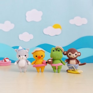 Puede incluir: Cuatro figuras amigurumi de ganchillo: un gato gris, un pato amarillo, una rana verde y un mono marrón. El gato lleva un gorro de marinero, el pato tiene un sombrero para el sol y un flotador rosa, la rana tiene un sombrero y una cesta, y el mono surfea en una tabla amarilla.