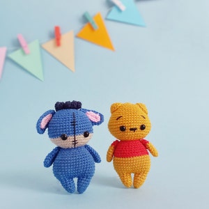 May include: Two crocheted stuffed toys, one blue with a stitched face and the other yellow with a red shirt, on a light blue background.