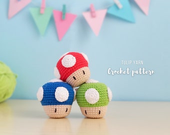 May include: Three crocheted mushroom plushies in red, blue, and green. The mushrooms are stacked on top of each other. The text "TULIP YARN Crochet pattern" is visible in the background.