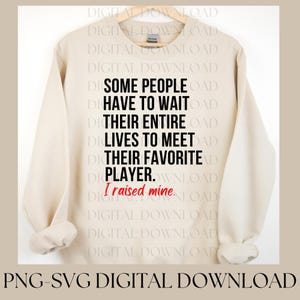 May include: A beige sweatshirt with long sleeves. The front of the sweatshirt features the text: "SOME PEOPLE HAVE TO WAIT THEIR ENTIRE LIVES TO MEET THEIR FAVORITE PLAYER. I raised mine."