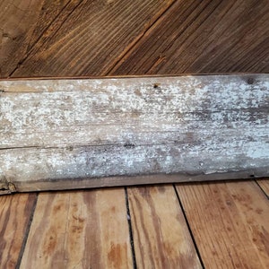 May include: A weathered, whitewashed wood plank with a rustic, distressed look. The plank is approximately 45 cm long and 15 cm wide. It has a natural wood grain and shows signs of age and use.