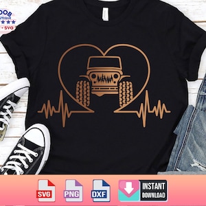 May include: A black t-shirt with a gold heart design featuring a jeep inside. The heart has a heartbeat line on either side. The t-shirt is laid out on a wooden surface with a pair of black sneakers and a pair of blue jeans.