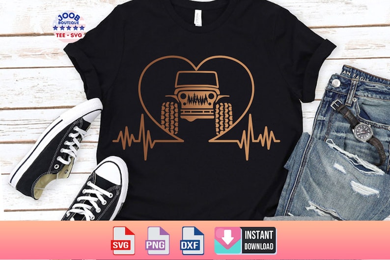 May include: A black t-shirt with a gold heart design featuring a jeep inside. The heart has a heartbeat line on either side. The t-shirt is laid out on a wooden surface with a pair of black sneakers and a pair of blue jeans.