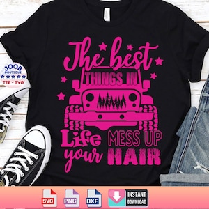 May include: A black t-shirt with a pink graphic design that says "The best things in life mess up your hair". The graphic also includes a pink Jeep with trees in the grill. The t-shirt is laying on a wooden surface with a pair of black sneakers and a pair of blue jeans.