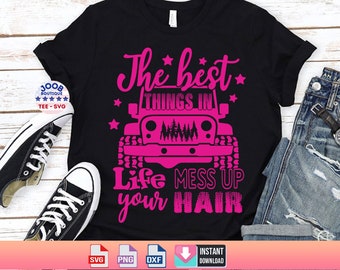 May include: A black t-shirt with a pink graphic design that says "The best things in life mess up your hair". The graphic also includes a pink Jeep with trees in the grill. The t-shirt is laying on a wooden surface with a pair of black sneakers and a pair of blue jeans.