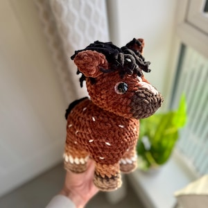 May include: A brown and black crocheted horse plush toy with white accents. The horse has a black mane and tail and large brown eyes.