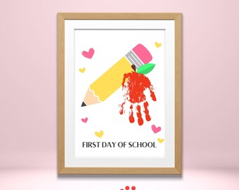 May include: A framed print with a yellow pencil, a red handprint shaped like an apple, and the text "FIRST DAY OF SCHOOL". The background is white with pink and yellow hearts.