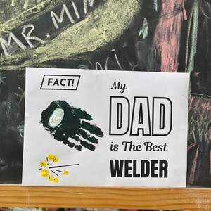 May include: A white card with black text that reads "FACT!" and "My Dad is The Best Welder". There is a green handprint and a yellow sparkler on the card.