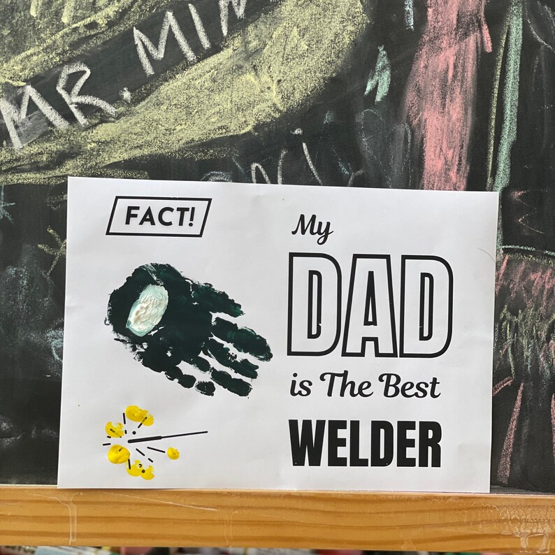 May include: A white card with black text that reads "FACT!" and "My Dad is The Best Welder". There is a green handprint and a yellow sparkler on the card.