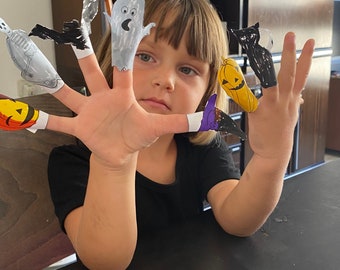 以下が含まれることがあります： 子供は指に指人形をつけています。人形はハロウィーンをテーマにしており、幽霊、カボチャ、魔女、猫、骸骨が含まれています。