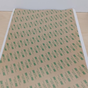 May include: A sheet of brown adhesive tape with a repeating pattern of green 3M logos. The tape is designed for mounting and securing objects.