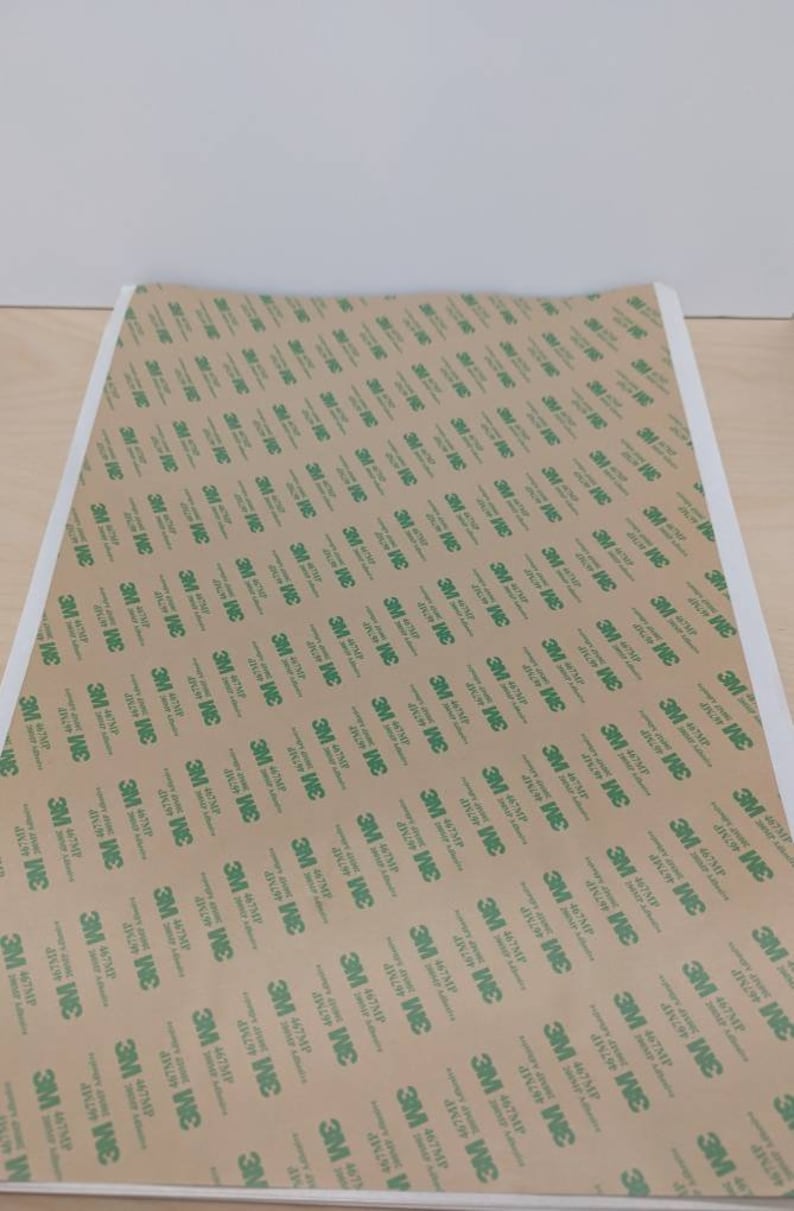 May include: A sheet of brown adhesive tape with a repeating pattern of green 3M logos. The tape is designed for mounting and securing objects.
