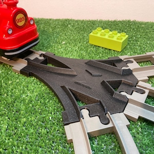 Peut inclure: Un train jouet rouge avec le numéro 925 sur le côté est sur une voie grise. Un aiguillage noir est au centre. Un bloc de construction jaune est sur la surface verte.