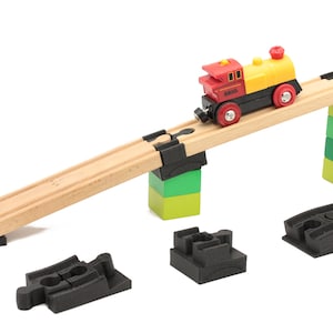 Könnte beinhalten: Ein Holz-Spielzeug-Eisenbahnset mit einer roten und gelben Spielzeug-Lokomotive. Die Schienen sind aus Holz und haben schwarze Kunststoff-Verbindungsstücke. Der Zug befindet sich auf einer Rampe aus Holz und schwarzem Kunststoff.