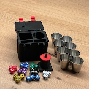 Könnte beinhalten: Ein schwarzer Kunststoffkoffer mit roten Verschlüssen, der ein Set mit Schnapsgläsern und Würfeln enthält. Der Koffer hat Fächer zur Organisation der Gegenstände. Die Würfel sind mehrfarbig und die Schnapsgläser sind silberfarben.