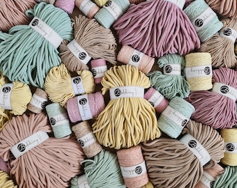 May include: A collection of pastel-coloured macrame yarn bundles and spools. The colours include pink, yellow, green, and beige. Each bundle is labelled with the brand name "Bobbing". The yarn is arranged in a textured pattern, creating a visually appealing display.