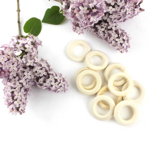 May include: A group of 10 off-white wooden rings, arranged in a loose pile on a white surface. The rings are all the same size and have a smooth, polished finish.