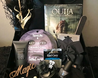 Könnte beinhalten: Schwarze Geschenkbox mit einem Ouija-Brettspiel, Gesichtsmasken, einer Nagelfeile, einer Schleife, einer Kerze und Nagellack. Die Box enthält auch ein Holzschild mit dem Wort "Magic".