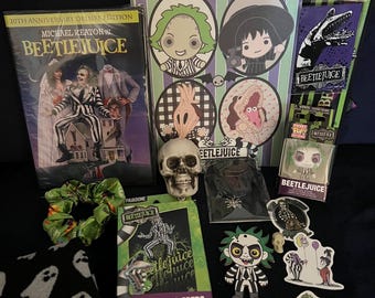 May include: A collection of Beetlejuice merchandise including a 20th Anniversary DVD, a spiral-bound notebook with character illustrations, a lanyard, a small skull, a scrunchie, black ghost-patterned fabric, playing cards, stickers, and a figure.