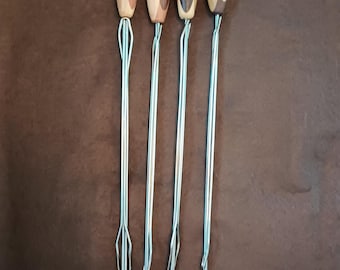 May include: Four metal roasting forks with wooden handles. The handles are made of various wood grains and colors, including light and dark brown. Each fork has a loop at the end of the handle and a three-pronged fork at the other end.