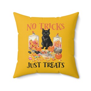 Puede incluir: Un coj&iacute;n cuadrado amarillo con un dise&ntilde;o de Halloween. Presenta un gato negro, calabazas y tarros de caramelos. El texto "NO TRICKS JUST TREATS" est&aacute; impreso en naranja.