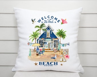 May include: White cushion with a blue beach house illustration, palm trees, and the text "Welcome to Our Beach House".