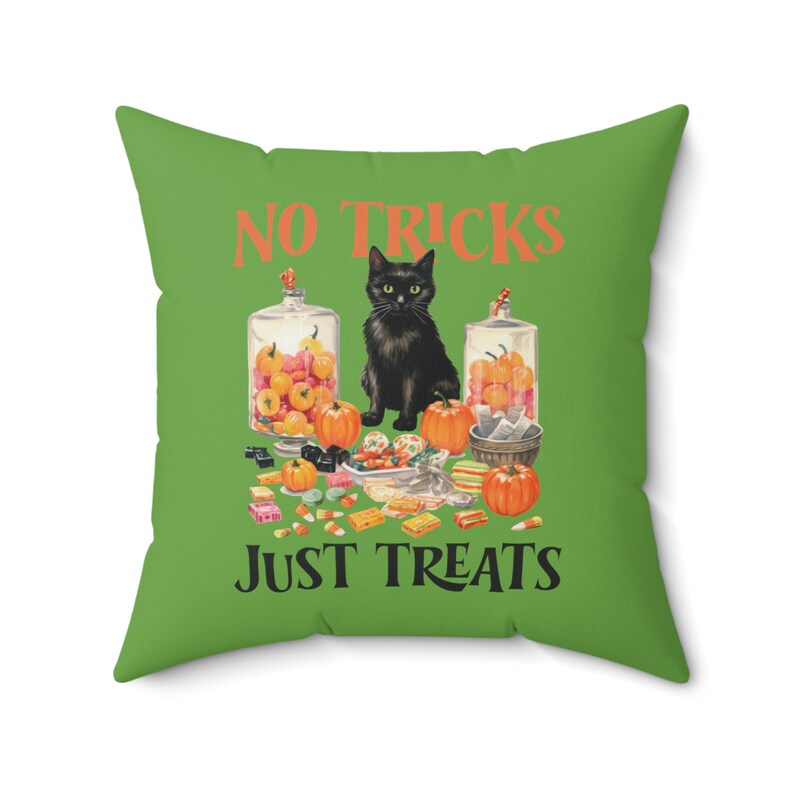 Puede incluir: Coj&iacute;n cuadrado verde con el texto "NO TRICKS JUST TREATS" en naranja. Presenta un gato negro, calabazas y botes de caramelos, ideal para la decoraci&oacute;n de Halloween.
