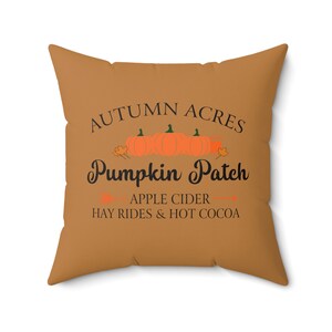 May include: A brown throw pillow with the text "Autumn Acres Pumpkin Patch" in black. Below the text is "Apple Cider Hay Rides & Hot Cocoa" in black.
