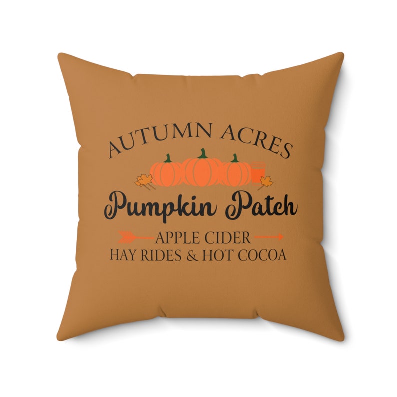 May include: A brown throw pillow with the text "Autumn Acres Pumpkin Patch" in black. Below the text is "Apple Cider Hay Rides & Hot Cocoa" in black.