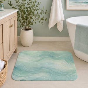 May include: A rectangular bath mat with a watercolor wave design in shades of blue and green. The mat is placed on a bathroom floor, near a white bathtub and a wooden cabinet.