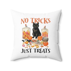 Puede incluir: Coj&iacute;n cuadrado blanco con un dise&ntilde;o tem&aacute;tico de Halloween. La imagen presenta un gato negro, calabazas y tarros de caramelos. El texto dice "NO TRICKS JUST TREATS" en naranja y negro.