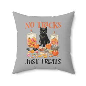 Puede incluir: Un coj&iacute;n cuadrado gris con el texto "NO TRICKS JUST TREATS" en naranja y negro. El coj&iacute;n presenta un gato negro, calabazas y tarros de caramelos, creando un tema de Halloween.