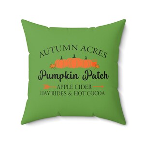 May include: Green cushion with the text "Autumn Acres Pumpkin Patch" in black lettering. The text is surrounded by a row of orange pumpkins and green leaves. Below the text is "Apple Cider Hay Rides & Hot Cocoa" in black lettering.