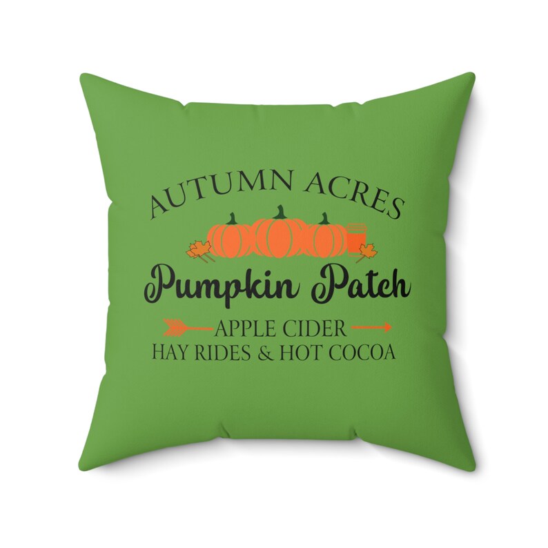 May include: Green cushion with the text "Autumn Acres Pumpkin Patch" in black lettering. The text is surrounded by a row of orange pumpkins and green leaves. Below the text is "Apple Cider Hay Rides & Hot Cocoa" in black lettering.