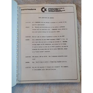 Pu&ograve; includere: Pagina di libro aperta con il logo Commodore e testo. La pagina contiene domande e risposte sui computer Commodore, tra cui grafica, stampa e notazione scientifica. Il testo &egrave; in nero.
