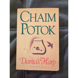 May include: A book cover with a woodgrain background. The title "Chaim Potok" is in green text. The book title "Davita's Harp" is in red text. A small bird and a harp are illustrated on the cover.