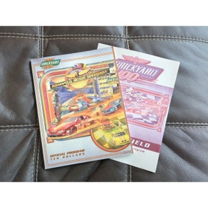 May include: Two program guides for the Brickyard 400 race at the Indianapolis Motor Speedway. The front cover of the guide on the left features a colorful illustration of race cars on the track. The guide on the right has a red, white, and blue color scheme with the text "Brickyard 400" in a large font.