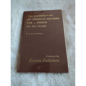 Op de afbeelding: Een bruin boek met de titel "The Handwriting of American Records for a Period of 300 Years" door E. Kay Kirkham. Uitgegeven door Everton Publishers. De omslag is effen bruin.