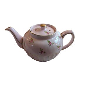May include: A pink teapot with a floral pattern and gold accents. The teapot has a round body and a spout on the side. The lid has a small knob on top.
