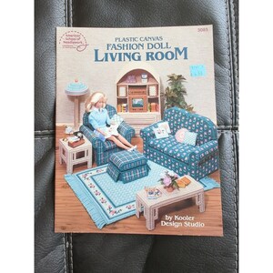 May include: Plastic canvas pattern for a fashion doll living room. The pattern includes a sofa, armchair, ottoman, coffee table, end table, rug, and a doll sitting in the armchair. The pattern is by Kooler Design Studio.