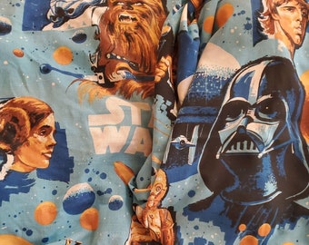 May include: A blue and white Star Wars themed fabric with images of Chewbacca, Darth Vader, Princess Leia, and R2-D2. The fabric has a blue background with white stars and the words "Star Wars" printed on it.