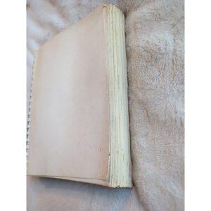 Pu&ograve; includere: Un quaderno a spirale con pagine invecchiate, bianco sporco. Le pagine sono leggermente ingiallite, a suggerire l'et&agrave; o l'uso. La copertina &egrave; di un colore bianco sporco simile. Il quaderno &egrave; aperto.