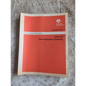 May include: A red instruction book for the Rockwell International ANS-351 Area Navigation Computer.