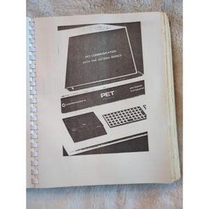 Pu&ograve; includere: Una pagina di un manuale vintage con un personal computer Commodore PET. L'immagine mostra uno schermo di computer con la scritta "PET COMMUNICATION WITH THE OUTSIDE WORLD", una tastiera e il logo Commodore. Il manuale &egrave; rilegato a spirale.