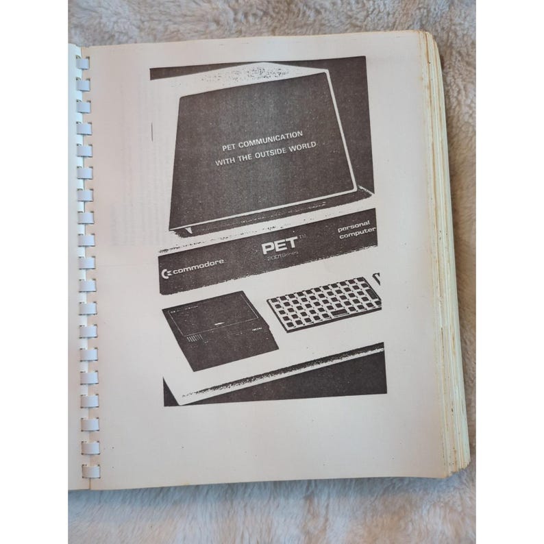 Pu&ograve; includere: Una pagina di un manuale vintage con un personal computer Commodore PET. L'immagine mostra uno schermo di computer con la scritta "PET COMMUNICATION WITH THE OUTSIDE WORLD", una tastiera e il logo Commodore. Il manuale &egrave; rilegato a spirale.