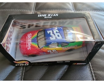 Puede incluir: Un coche de juguete de metal rojo, amarillo, verde y azul con el número 36 en el lateral. El coche es una réplica del coche de carreras NASCAR de Ernie Irvan patrocinado por Skittles.