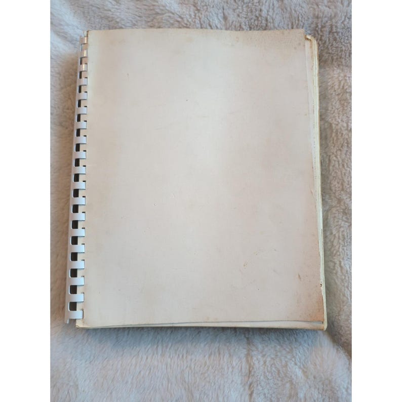 Pu&ograve; includere: Un quaderno a spirale aperto, con pagine bianco sporco. Il quaderno &egrave; aperto, rivelando pagine vuote. La rilegatura &egrave; nera e le pagine sono leggermente ingiallite. Il quaderno &egrave; appoggiato su una superficie strutturata.