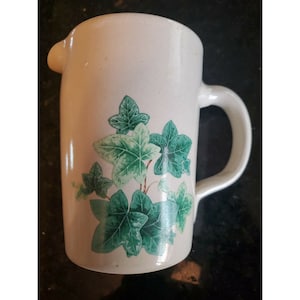 以下が含まれることがあります： 緑色のツタの葉のデザインが施された白いセラミックピッチャー。