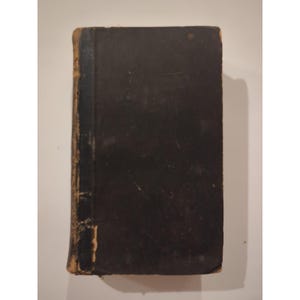May include: A vintage, rectangular book with a dark brown cover. The spine and edges show signs of wear, with a lighter brown color. The book appears to be old, with a slightly distressed appearance.