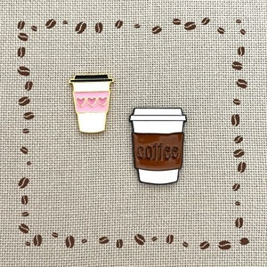 May include: Two enamel pins shaped like coffee cups. One cup is white with pink hearts and the other is white with brown coffee and the word "coffee" printed on it.